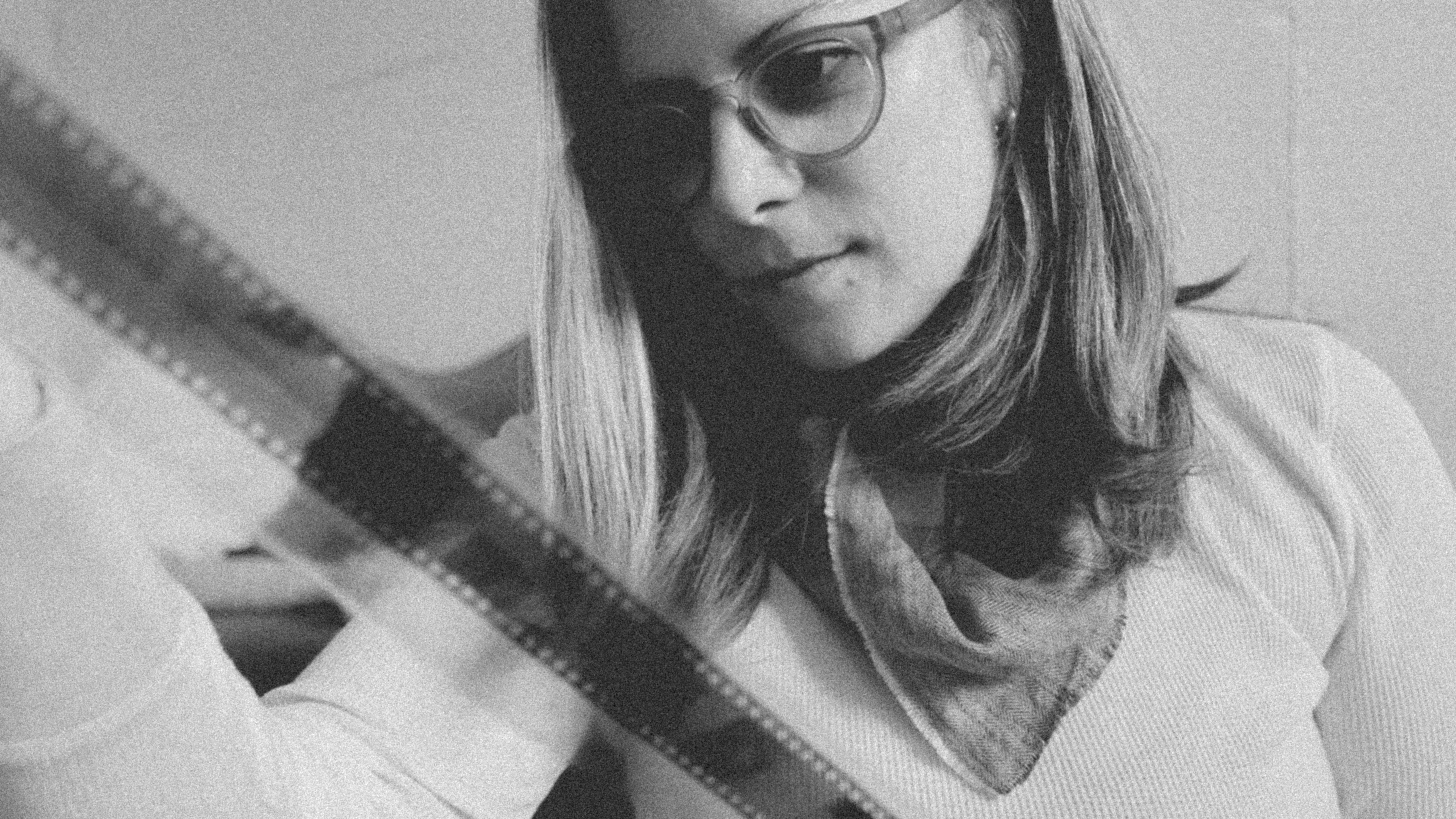 Black-and-white portrait of a female photographer, Coley Cary, reviewing a strip of film.